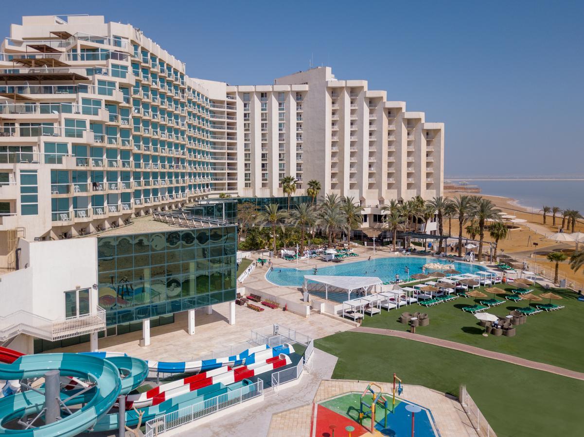 Leonardo Club Hotel Dead Sea Неве-Зогар Екстер'єр фото The image shows a large hotel complex alongside a pool area. The hotel features modern architecture with multiple levels and numerous balconies. In front of the hotel, there is a recreational area with a swimming pool, water slides, and lounging chai
